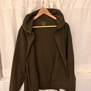Olivgrön hoodie från Polo Ralph Lauren - Säljer en olivgrön hoodie från Polo Ralph Lauren i bomull. Tröjan har dragkedja framtill, huva och fickor samt en broderad logga på bröstet. Perfekt för en avslappnad stil.