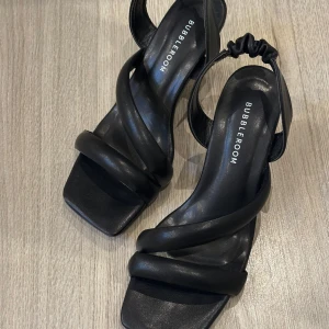 Svarta klackskor från Bubbleroom - Säljer ett par svarta klack från Bubbleroom med trendig fyrkantig tå. Skorna har breda remmar och elastisk detalj vid hälen för extra komfort. Perfekta för att lyfta din outfit med en stilren touch.