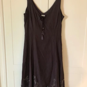 Brun festklänning i silke - Brun festklänning i silke med pärlbroderi nertill. Knytning fram. Isydd underklänning och dold dragkedja i sidan. Längden från axel till nederkant är 110 cm.  Sparsamt använd. Strl M motsvarar ca strl 40. 