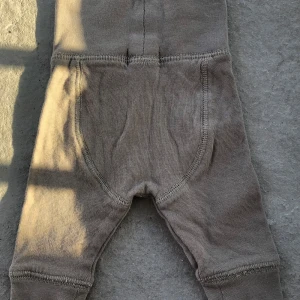 Beige mjukisbyxor från Newbie med knappar - Beiga mjukisbyxor från Newbie i mjukt bomullsmaterial. Byxorna har två dekorativa knappar framtill och bred mudd i midjan för extra komfort. Perfekta för en avslappnad och bekväm stil.