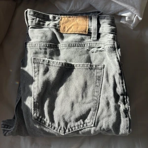 Grå jeans från Zara med råa benslut - Säljer ett par grå jeans från Zara med raka ben och råa, fransiga benslut. Jeansen har klassisk femficksdesign och en liten sliten detalj ovanför bakfickan. Använda med lite sönder vid fickan sen och sliten vid benen 