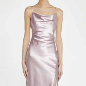 Ljusrosa långklänning i satin med slits - Elegant ljusrosa långklänning i glansigt satinmaterial med smala axelband och slits framtill. Klänningen har en mjukt draperad urringning och figurnära passform som faller snyggt längs kroppen. Perfekt till balen!