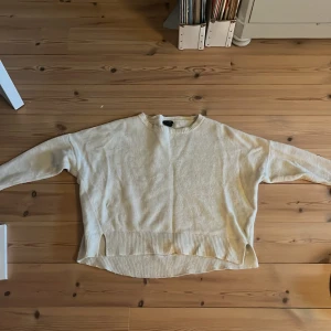 Beige stickad tröja från Lindex - Mysig beige stickad tröja från Lindex med rund halsringning och ribbade muddar vid ärmslut och nederkant. Tröjan har en avslappnad passform och är perfekt för lager-på-lager-stil.