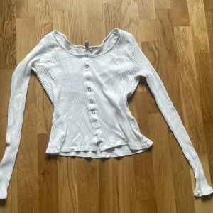 Vit ribbad långärmad topp med knappar - Säljer en vit ribbad långärmad topp med knappar framtill. Toppen har en rundad halsringning och är tillverkad i ett mjukt, stretchigt material. Perfekt att styla till jeans eller kjol. 