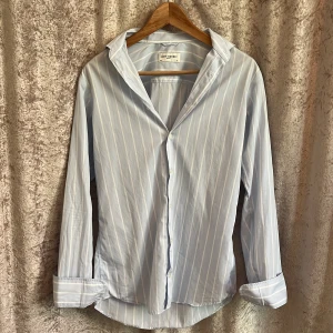 Ljusblå randig skjorta från John Henric - Snygg ljusblå skjorta från John Henric med vita ränder och klassisk krage. Skjortan har långa ärmar och knappar framtill. Perfekt för en stilren och fräsch look nu till sommaren!! Skick 9,9/10 då den aldrig har kommit till användning. Storlek XS. Nypris 1000 kr
