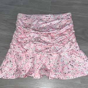 Rosa blommig kjol från SHEIN - Supersöt rosa kortkjol från SHEIN med blommigt mönster och volang nertill. Kjolen har rynkade detaljer framtill och är tillverkad i ett mjukt syntetmaterial. Perfekt för dig som gillar en feminin och lekfull stil! Helt ny, har bara testat den inget mer!