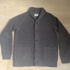 Grå cardigan  - Mysig grå stickad kofta från Tokyo Laundry med knappar framtill och två fickor. Perfekt för lager-på-lager och har en klassisk, enkel design med ribbade muddar och krage. Cardigan är köpt på BESTSECRET för 900kr och den är knappast använd.