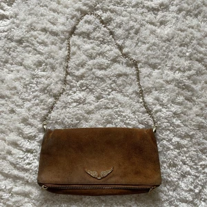 Brun axelväska i mocka från Zadig & Voltaire - Säljer en snygg brun axelväska i mocka från Zadig & Voltaire med guld detaljer. Finns defekter (bild 4) samt lite missfärgad men gör säkert att fräscha till. Skriv för frågor eller diskutera pris💖