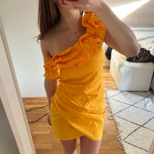 Orange klänning med volang - Superfin orange klänning med one shoulder och volang. Perfekt till sommaren! Storlek: XS