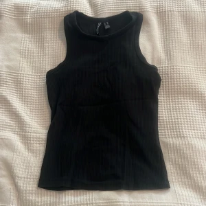 Svart ribbad linnetopp från Pieces - Säljer en svart ribbad linnetopp från Pieces. Toppen har en tight passform och är ärmlös med rund halsringning. Perfekt för sommaren och enkel att matcha med olika outfits. 🫶🏼🫶🏼