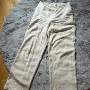 Beige linnebyxor från Object - Säljer ett par beige linnebyxor från Object med resår i midjan och raka, vida ben. Byxorna har diskreta fickor i sidorna och är tillverkade i ett luftigt linnematerial, perfekta för varmare dagar.