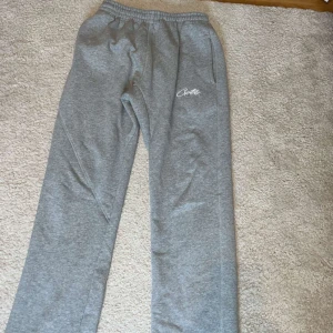 Grå mjukisbyxor från Corteiz - Säljer ett par grå mjukisbyxor från Corteiz i Storlek M med vit logga på ena benet. Byxorna har resår i midjan med snörning och raka ben. Perfekta för en avslappnad stil. för fler bilder kom privat pris kan diskuteras 