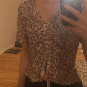 Blus - Säljer en söt blommig blus i ljusa färger med lila, rosa och orange toner. Toppen har korta ärmar, v-ringning och knyt framtill. Toppen är från chiquelle och har bara använts en gång! Storleken är lite stor så det passar även dig som har S eller M 🫶 kontakta vid intresse 