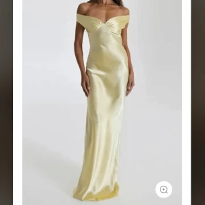 Ljus gul långklänning i satin - Elegant balklänning/långklänning i skimrande ljus gul satin med offshoulder-skärning och lätt v-ringad detalj framtill. Klänningen har figurnära passform och släpper mjukt längs kroppen för en lyxig känsla. Nypris 1148 kr