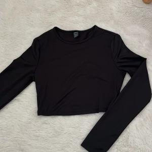 Svart croppad långärmad topp från SHEIN - Säljer en svart croppad långärmad topp från SHEIN. Enkel och stilren design med rund halsringning och tight passform. Materialet känns mjukt och stretchigt.