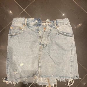 Ljusblå jeanskjol från Gina tricot - Ljusblå jeanskjol med slitna detaljer. Klassisk femficksmodell med knappgylf och hög midja. Perfekt för en avslappnad och trendig look. Knappt använd så i jättefint skick🌷