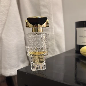 Parfym Paco Rabanne - Unik parfymflaska designad som en robot med gulddetaljer och svarta solglasögon. Flaskan har en genomskinlig kropp med mönstrad yta och guldinslag, vilket ger en futuristisk och lyxig känsla. Cirka 1/3 kvar. Därav det billiga priset 
