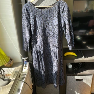 Blå spetsklänning från Soaked in Luxury - Säljer en blå klänning från Soaked in Luxury med vackert spetsmönster och trekvartsärm. Klänningen har rund halsringning och en liten öppning med knapp i ryggen. Perfekt för dig som vill ha en elegant look.