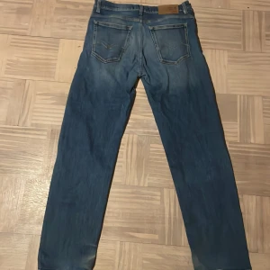Blå jeansbyxor från Replay - Säljer ett par klassiska blå jeans från Replay med raka ben och normal passform. Byxorna har fem fickor, dragkedja och knapp framtill samt Replay-logga på bakfickan och läderpatch i midjan.