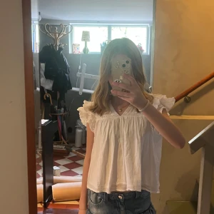 Vit blus med volangärmar - Säljer en söt vit blus med volangärmar och smockdetaljer upptill. Blusen har en lös passform och v-ringning, perfekt till sommaren. Superfin att matcha med jeans eller kjol! Från Gina tricot. Kan ksk förhandla om pris