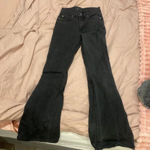 Svarta flare jeans - Säljer ett par svarta bootcut jeans med hög midja. Jeansen har klassisk femficksdesign och stängs med dragkedja och knapp. Perfekta för dig som gillar en retroinspirerad look med utsvängda ben.