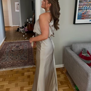 Champagnefärgad långklänning med halterneck - Säljer en elegant långklänning i champagnefärgat satin med halterneck och draperad överdel. Klänningen har öppen rygg och en figurnära passform. Perfekt för bal eller festliga tillfällen! Använd en gång💕nypris 1569kr men säljer för 1300kr🥂