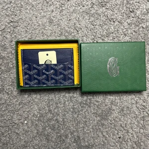 Blå korthållare från G|oyard - Säljer en blå korthållare från G|oyard med deras klassiska mönster i vitt och grått. Korthållaren har flera fack för kort och levereras i originalask med tillhörande och tagg. Perfekt för dig som vill ha en stilren och lyxig accessoar.