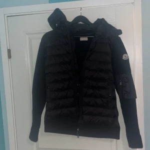 Moncler cardigan  - Söker BARA serösa köpare! Säljer en svart pufferjacka från Moncler med huva och dragkedja. Jackan har quiltad framsida och ärmar i stickad struktur. Klassisk Moncler-logga på ärmen och praktiska fickor framtill. Pris kan diskuteras.