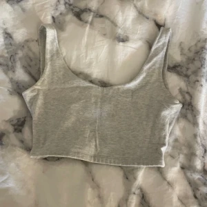 Grå croppad linnetopp - Säljer en stilren grå croppad linnetopp. Toppen är ärmlös och croppad, perfekt för varma dagar. Den har en enkel och bekväm design som passar till många olika outfits.