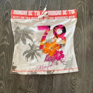 Vit tubtopp - Säljer en vit tubtopp från Morgan de Toi med färgglatt tryck av siffran 78 och blommor. Toppen har ett tropiskt mönster med palmer och en knytning upptill. Perfekt för sommardagar!