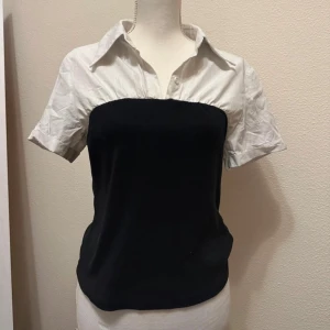 Svart och vit blus - Snygg blus med en unik design som kombinerar en vit krage och korta ärmar med en svart kropp. Perfekt för en stilren look.