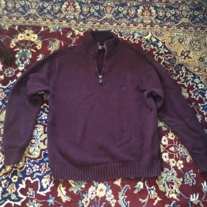 Vinröd tröja med dragkedja från Chaps - Säljer en vinröd tröja från Chaps i 100% bomull. Tröjan har en halv dragkedja vid halsen och ribbade muddar vid ärmslut och nederkant. Tröjan har ett hål på ena ärmen vid armbågen