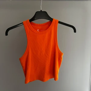 Orange ribbad linnetopp från FSBN Sister - Snygg orange ribbad linnetopp från FSBN Sister. Perfekt för varma dagar med sin ärmlösa design och croppade passform. Tillverkad i ett mjukt och bekvämt material.