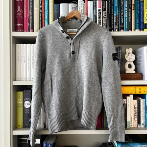 Grå tröja från Stone Island - Säljer en stilren grå tröja från Stone Island med knappar vid halsen och ribbade detaljer vid krage, ärmslut och nederkant. Material: ull.