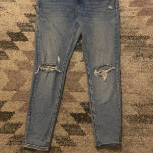 Blå jeans från Stradivarius - Snygga blå jeans från Stradivarius med slitna detaljer på knäna. De har en klassisk femficksdesign och knappgylf. Perfekta för en avslappnad stil.