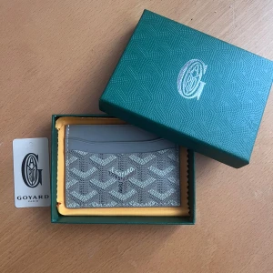 Grå plånbok - Säljer en elegant grå plånbok med deras ikoniska mönster. Plånboken har flera fack för kort och är perfekt för att hålla dina tillhörigheter organiserade. Kommer i en snygg grön förpackning.