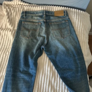 Blå tiger of sweden jeans - Säljer ett par klassiska blå jeansbyxor med en lätt slitning på framsidan. De har en rak passform och traditionella fem fickor. Perfekta för en avslappnad stil.