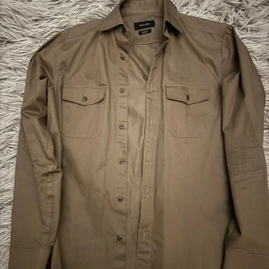 Massimo Dutti overshirt - Snygg brun overshirt från Massimo Dutti i 100% bomull. Skjortan har långa ärmar och två bröstfickor med knappar. Perfekt nu när de börjar bli lite varmare om dagarna! Bara att höra av sig vid minsta fundering
