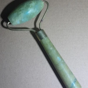 Jade sten ansiktsroller - Säljer en grön ansiktsroller i jade. Perfekt för att massera ansiktet och ge huden en fräsch känsla. Rollern har ett handtag och en rullande del som är lätt att använda. Perfekt för daglig hudvård.