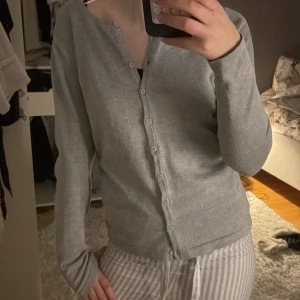 Grå kofta med knappar - Säljer en stilren grå kofta med knappar framtill. Perfekt för lager-på-lager och passar till många olika outfits. Koftan har långa ärmar och en klassisk design.