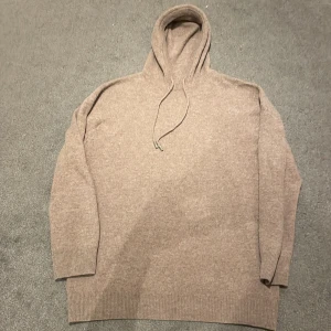 Beige stickad hoodie - Säljer en mysig beige stickad hoodie med ribbade muddar och dragsko i huvan. Perfekt för kyliga dagar och ger en avslappnad stil. Passar bra till jeans eller mjukisbyxor. 50/50 kashmir och merino ull