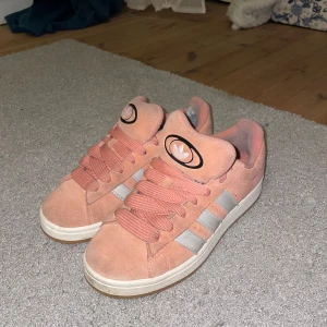 Adidas campus 00 rosa  - Snygga rosa adidas campus 00. Skorna har en bekväm passform och är perfekta för vardagsbruk. De har en gummisula och snörning framtill för en säker passform. Skorna har ett lätt slitage inuti bakre häl (syns på bild 1 och 3) men inget stort, endast tyget som gått litet hål på. (Därav priset) Annars bra skick!