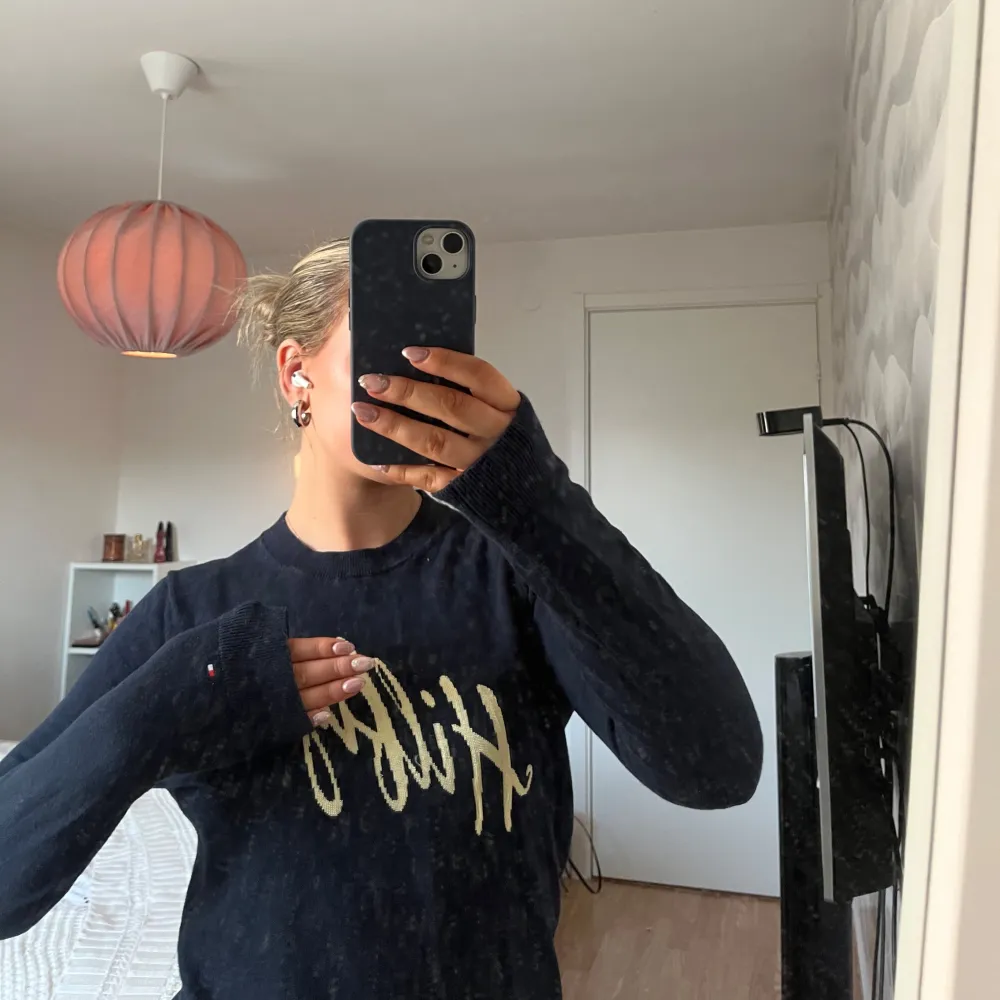 Säljer en marin blå tröja från Hilfiger med guldfärgad text på bröstet. Tröjan har långa ärmar och en klassisk passform. Perfekt för en stilren look.. Neuletakit & Villapaidat.