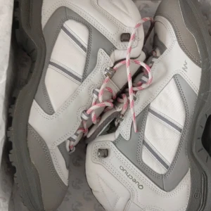 Vita och grå vandringskängor från Quechua - Robusta vandringskängor i vitt och grått med snörning och slitstark sula. Perfekta för utomhusaktiviteter med bra grepp och stöd. Designade för att klara tuff terräng och ge komfort under långa vandringar.