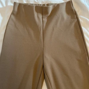 Brun/beige utsvängda byxor från H&M - Snygga beige byxor med hög midja och utsvängda ben från H&M i storlek XS. Perfekta för en stilren look. Tillverkade i ett mjukt och bekvämt material. Använd ett fåtal gånger och är i mycket bra skick. 