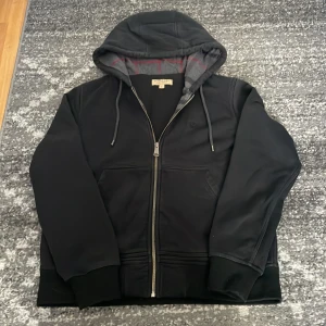 Svart huvtröja från Burberry - Säljer en svart huvtröja från Burberry med burberry mönster på insidan av tröjan. 