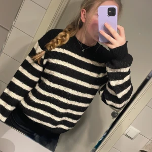 Svart och vit randig stickad tröja - Säljer en mysig svart och vit randig stickad tröja med långa ärmar. Perfekt för kyligare dagar och ger en stilren look. Tröjan har en klassisk passform och är lätt att matcha med olika outfits.