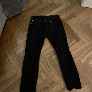 Svarta jeansbyxor från Levi's 501 - Snygga svarta jeansbyxor från Levi's 501 med klassisk design. Byxorna har en rak passform och är perfekta för en stilren look. De har fem fickor och knappar i gylfen.