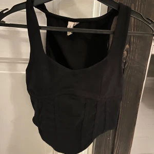 Svart korsetttop från Nelly - Snygg svart korsetttopp från Nelly med lite bredare axelband. Är i storlek XS och passar bra till både jeans och kjol! Aldrig använd! 🖤