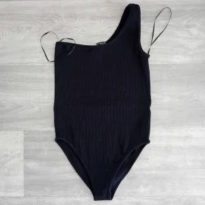Svart ribbad bodysuit från zara - Snygg svart bodysuit med en axel och ribbad design från Zara. I mycket bra skick ,storlek m-l